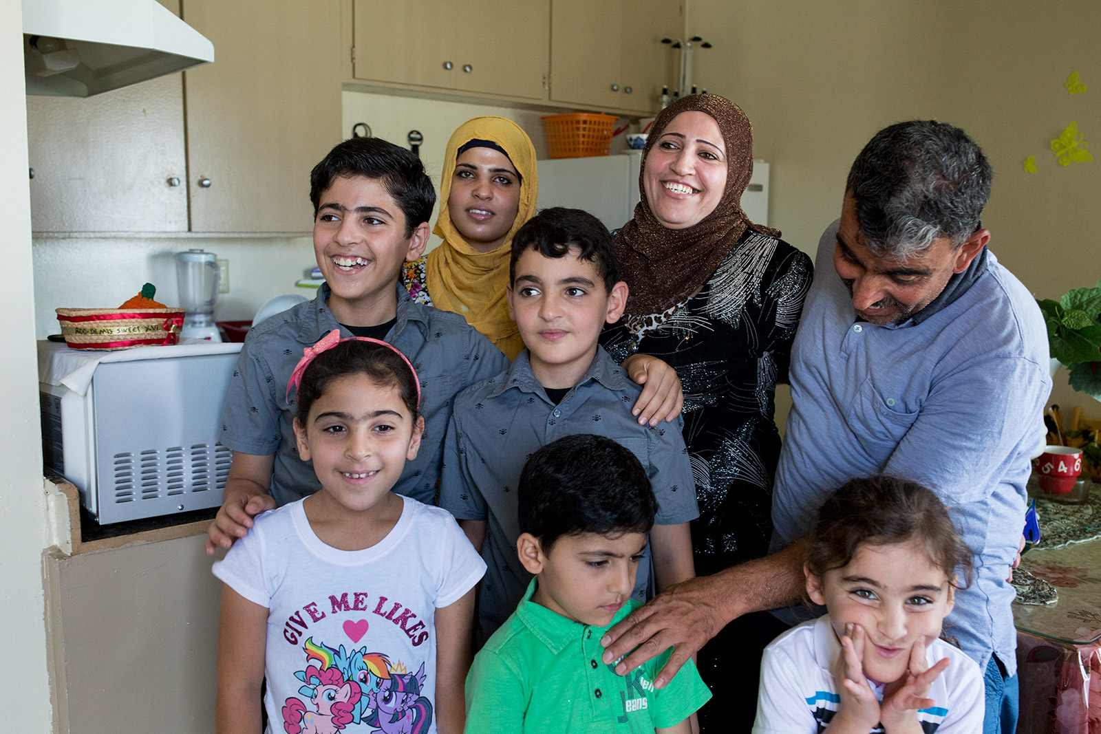 Mohamad Abdullah (far right), touches the shoulder of his son during a family photo in kitchen of the family's two-bedroom El Cajon apartment, July 25, 2017. Photo by Megan Wood, inewsource.